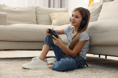 Photo of Happy girl in headphones playing video game on floor indoors