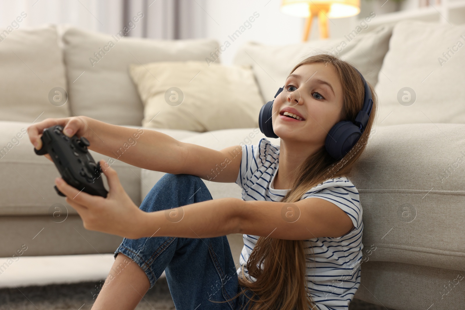 Photo of Happy girl in headphones playing video game on floor indoors