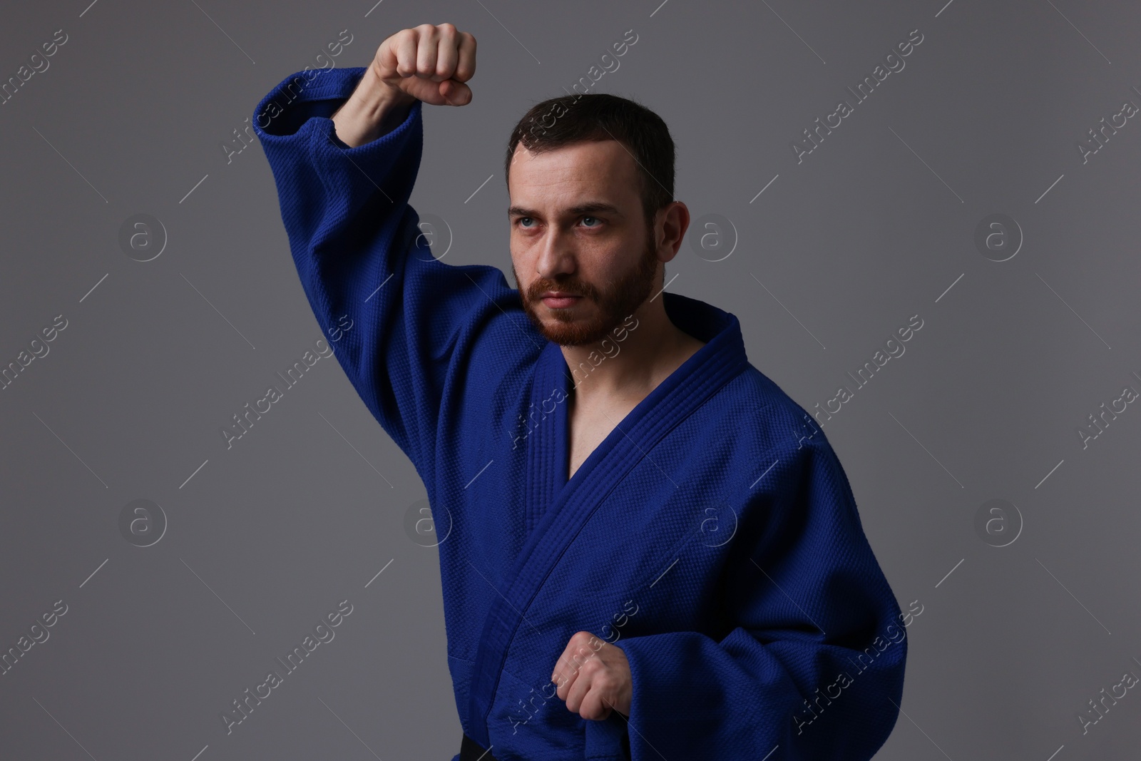 Photo of Man in uniform practicing karate on grey background