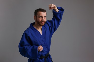 Photo of Man in uniform practicing karate on grey background