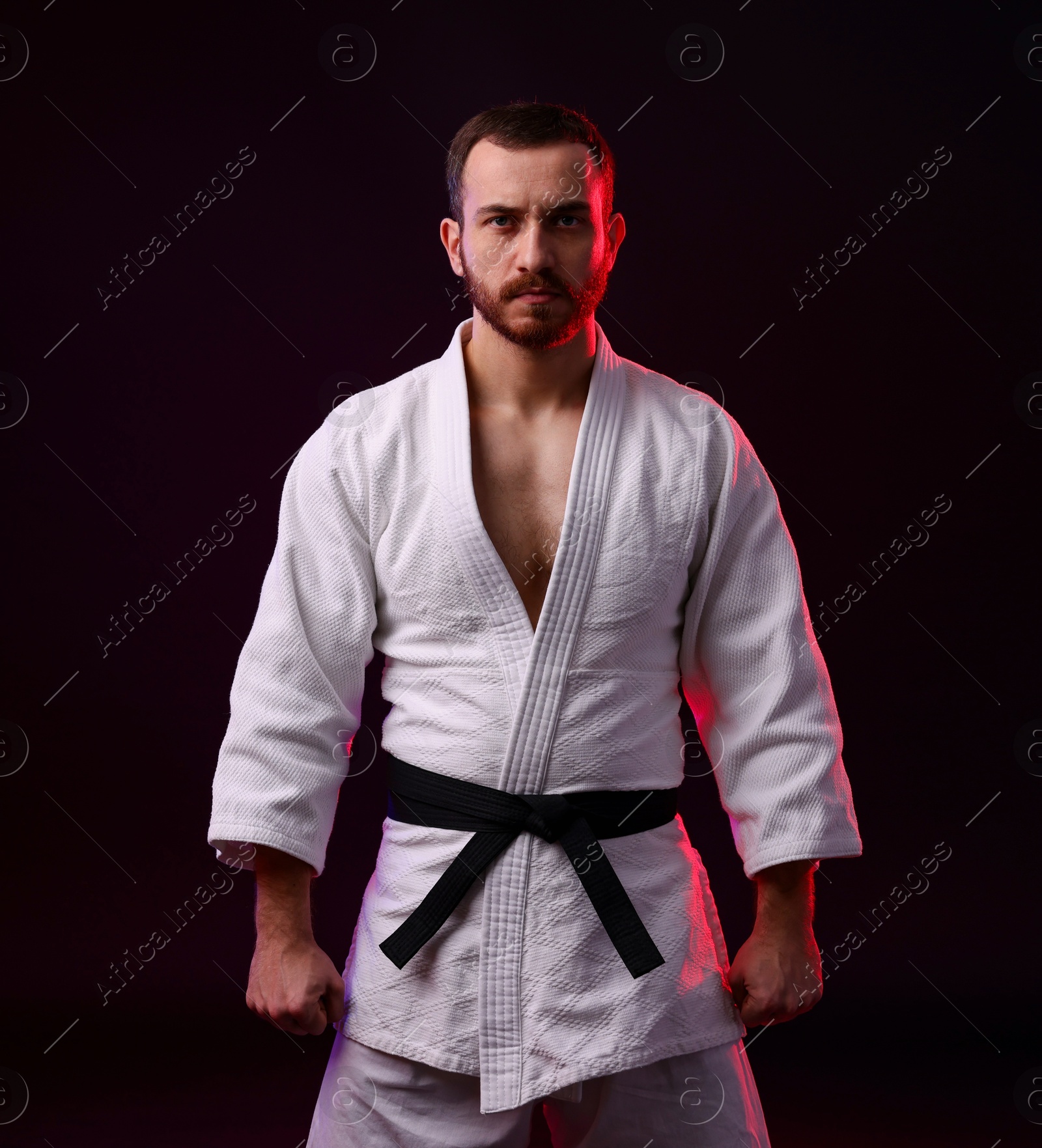 Photo of Karate fighter wearing uniform in color light against black background