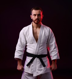 Photo of Karate fighter wearing uniform in color light against black background