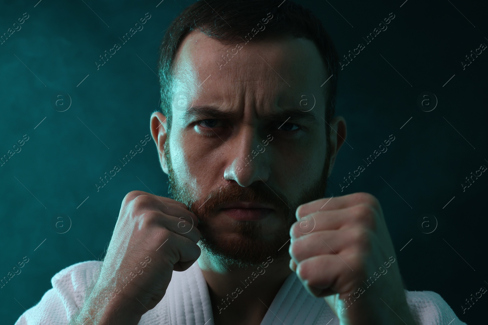 Photo of Karate fighter wearing uniform in color lights and smoke, closeup