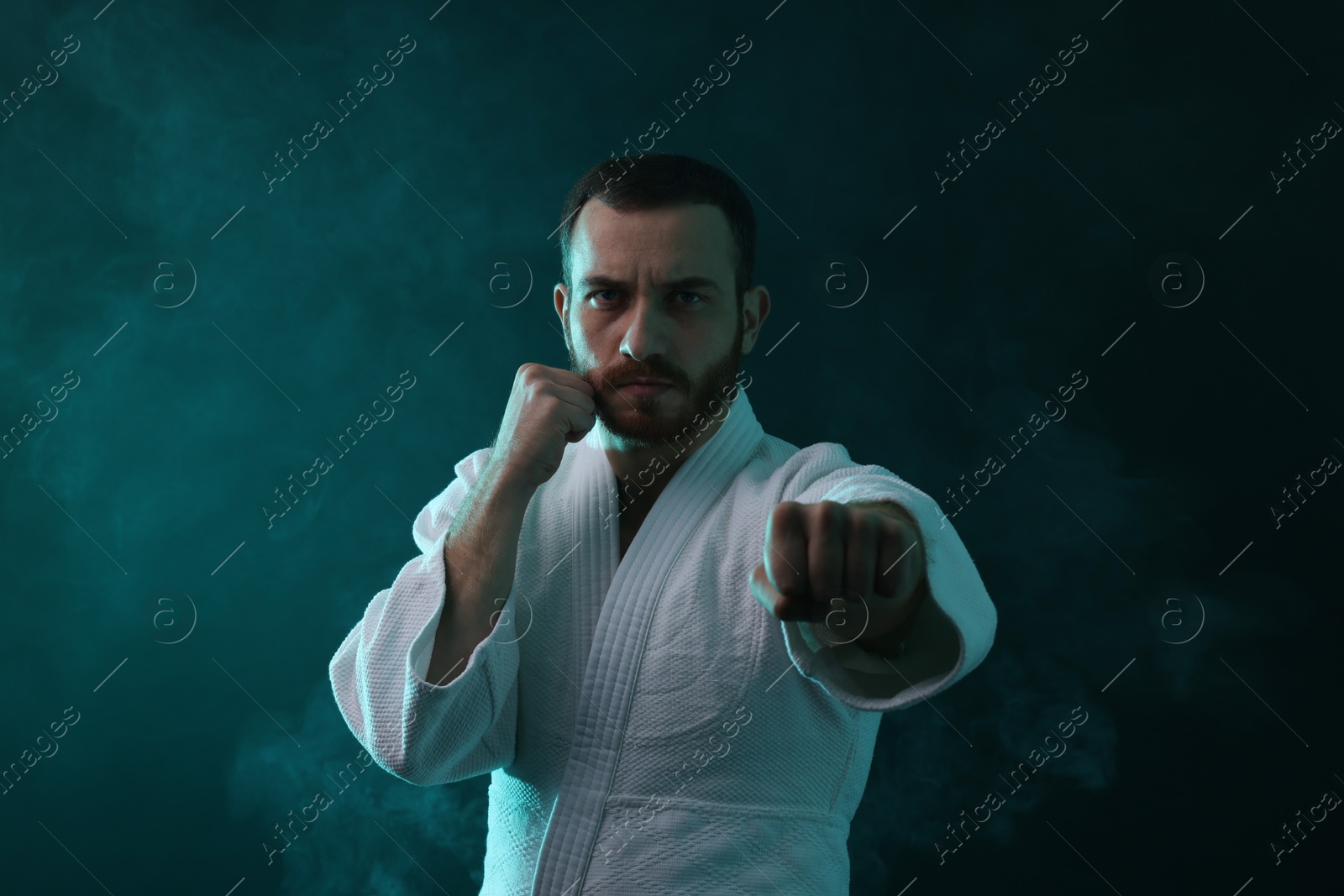 Photo of Man wearing uniform practicing karate in color lights and smoke