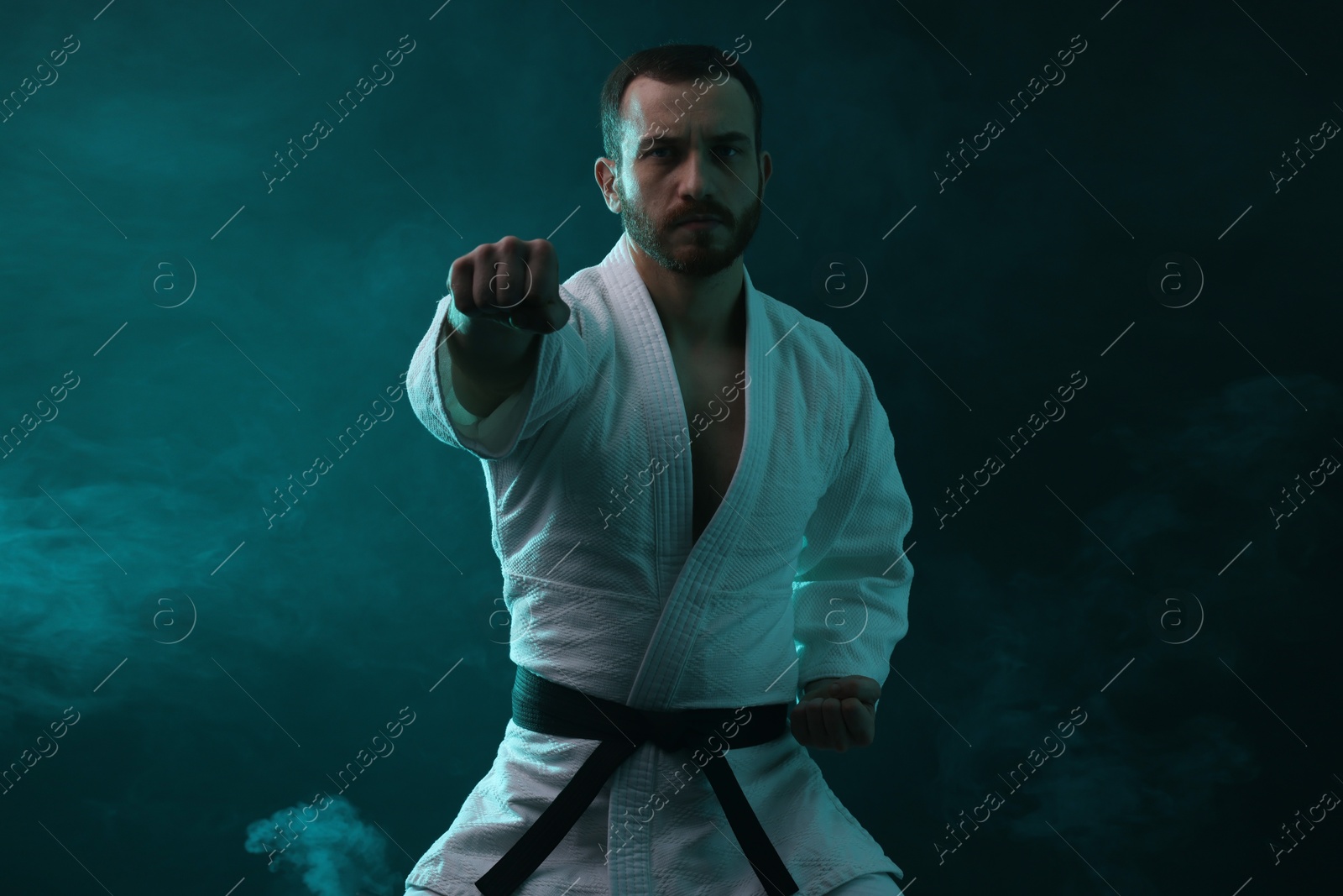 Photo of Karate fighter wearing uniform in color lights and smoke