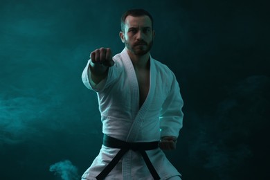 Photo of Karate fighter wearing uniform in color lights and smoke