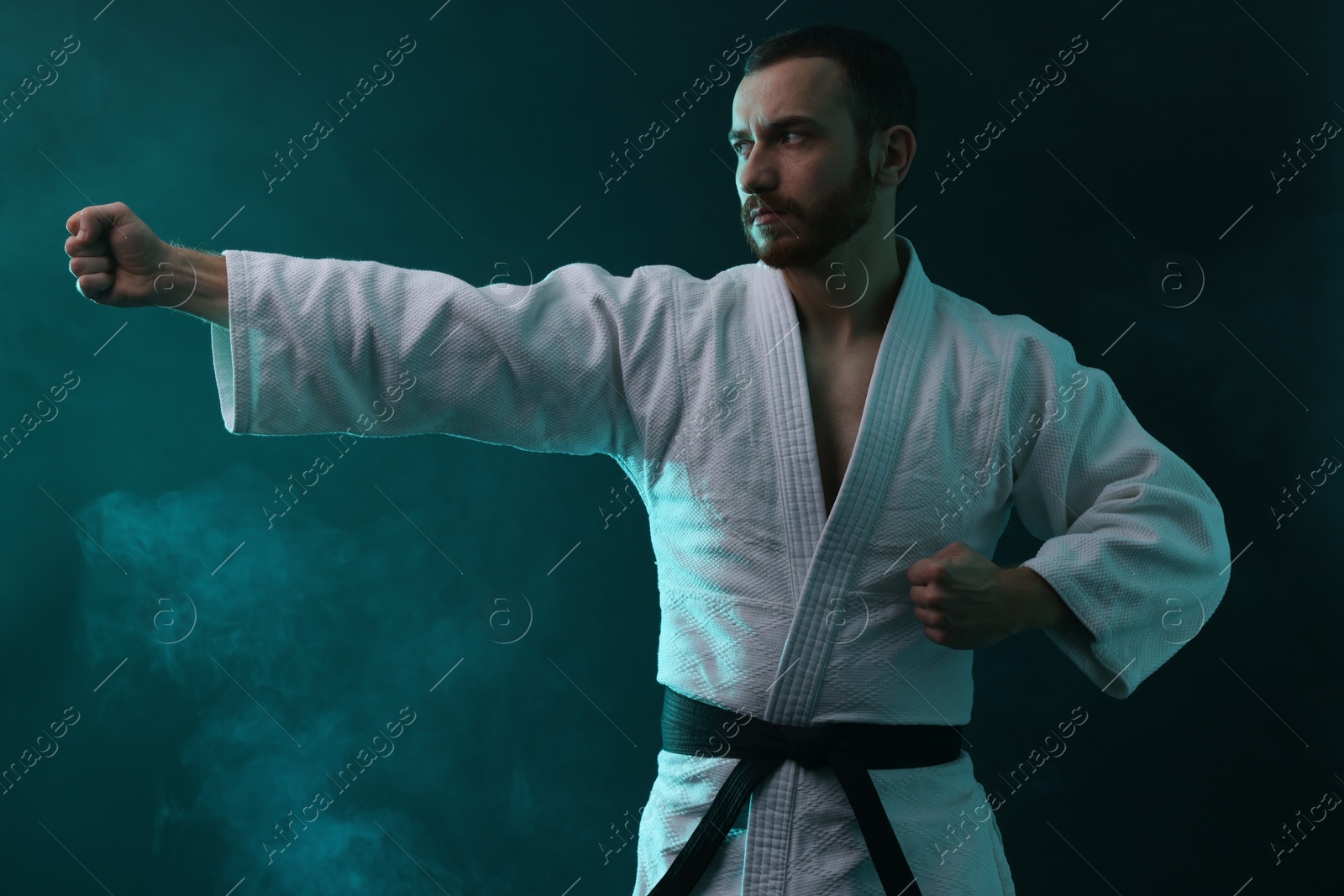 Photo of Man wearing uniform practicing karate in color lights and smoke