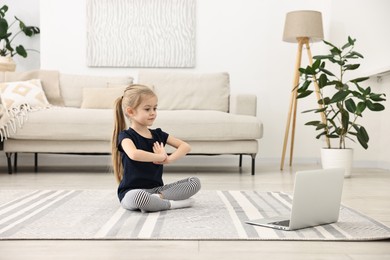 Photo of Little girl exercising with online coach via laptop at home. Sport activity