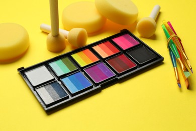 Photo of Face paints and tools on yellow background, closeup