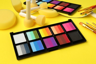 Photo of Face paints and tools on yellow background, closeup