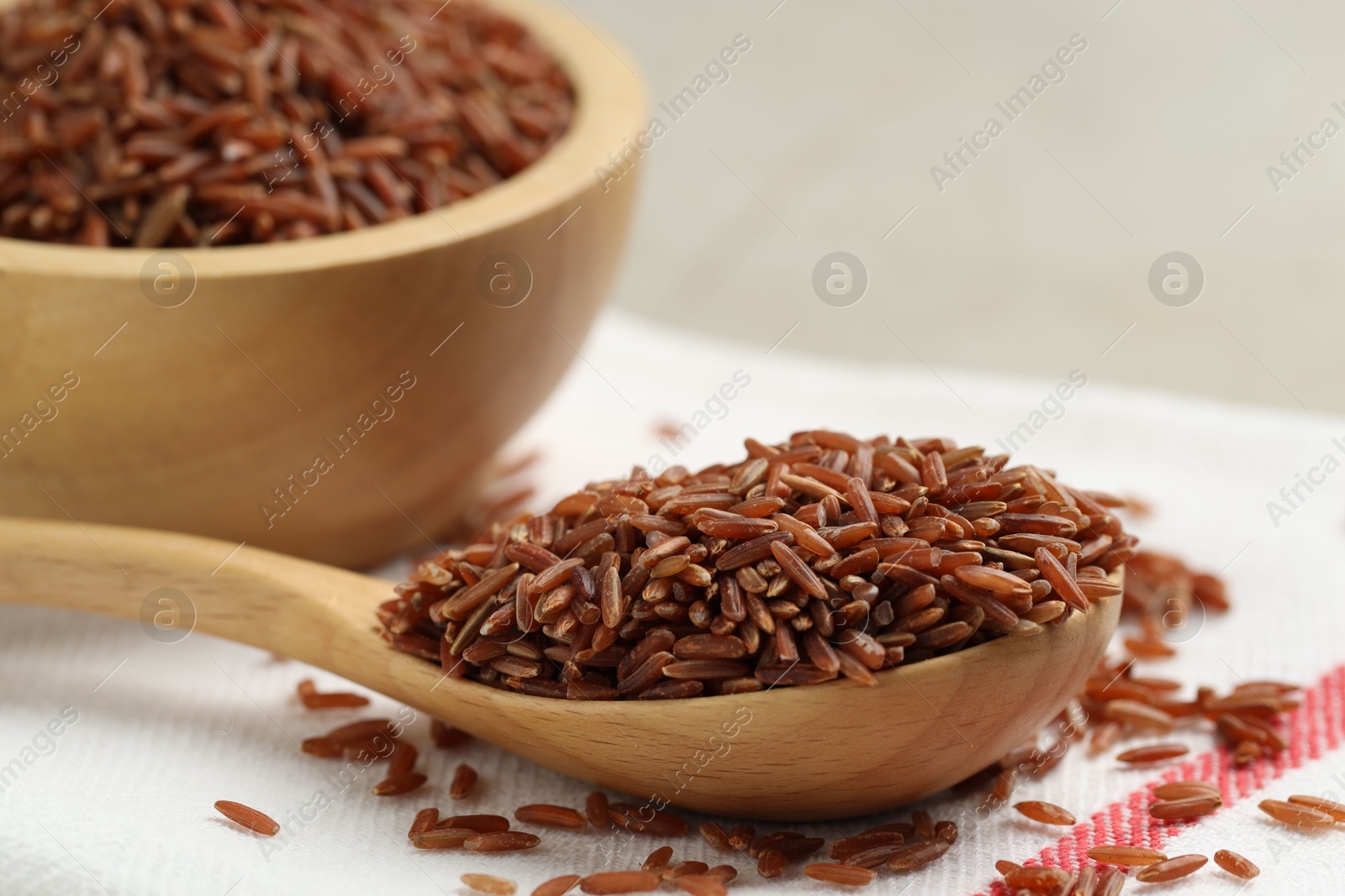 Photo of Brown rice in wooden spoon and bowl on table, closeup