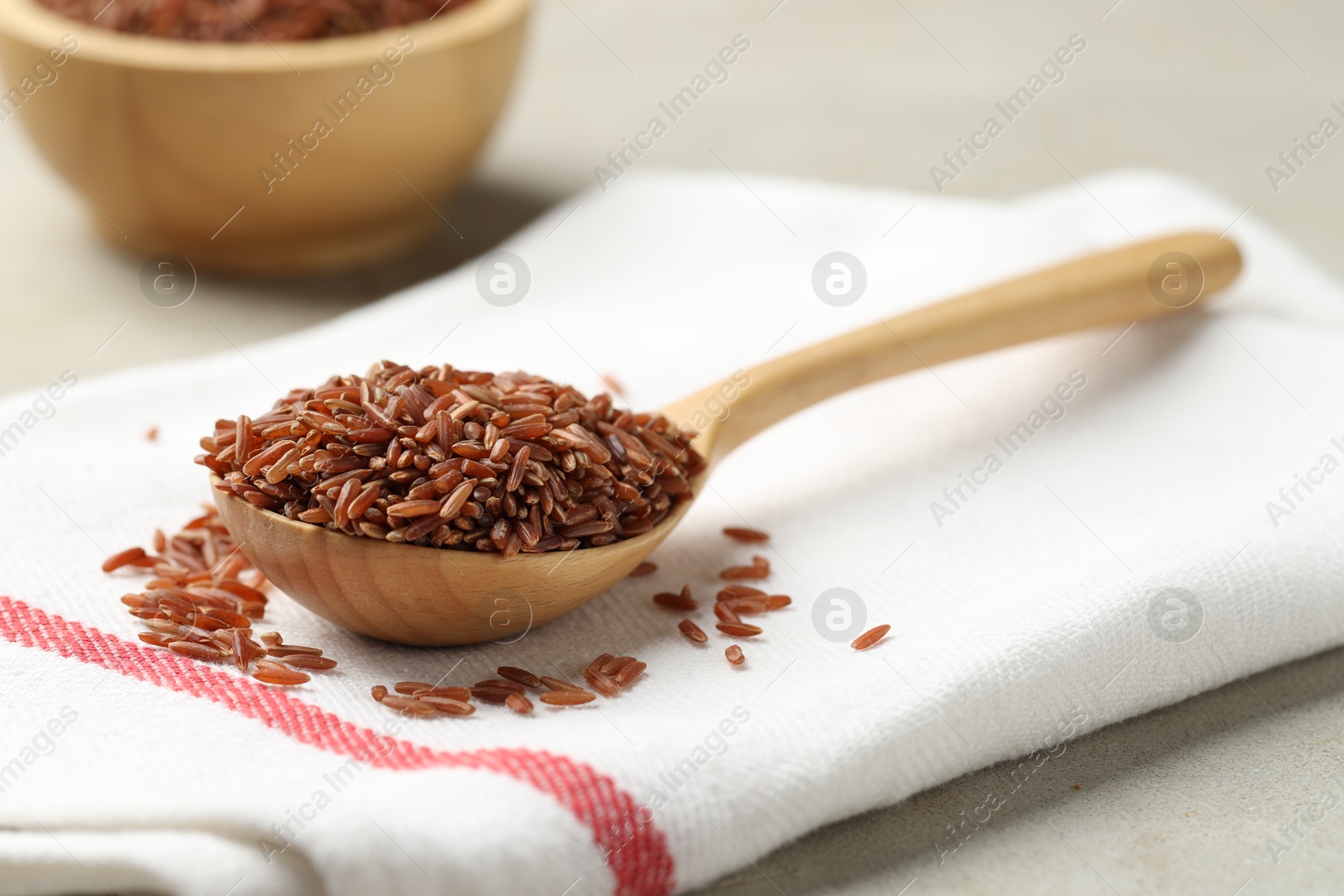 Photo of Brown rice in wooden spoon on light grey table, closeup