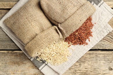 Photo of Different types of brown rice in sacks on wooden table, flat lay