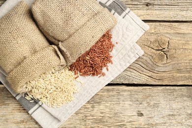 Photo of Different types of brown rice in sacks on wooden table, flat lay. Space for text