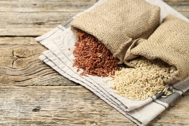 Photo of Different types of brown rice in sacks on wooden table, closeup. Space for text