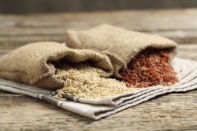 Photo of Different types of brown rice in sacks on wooden table, closeup