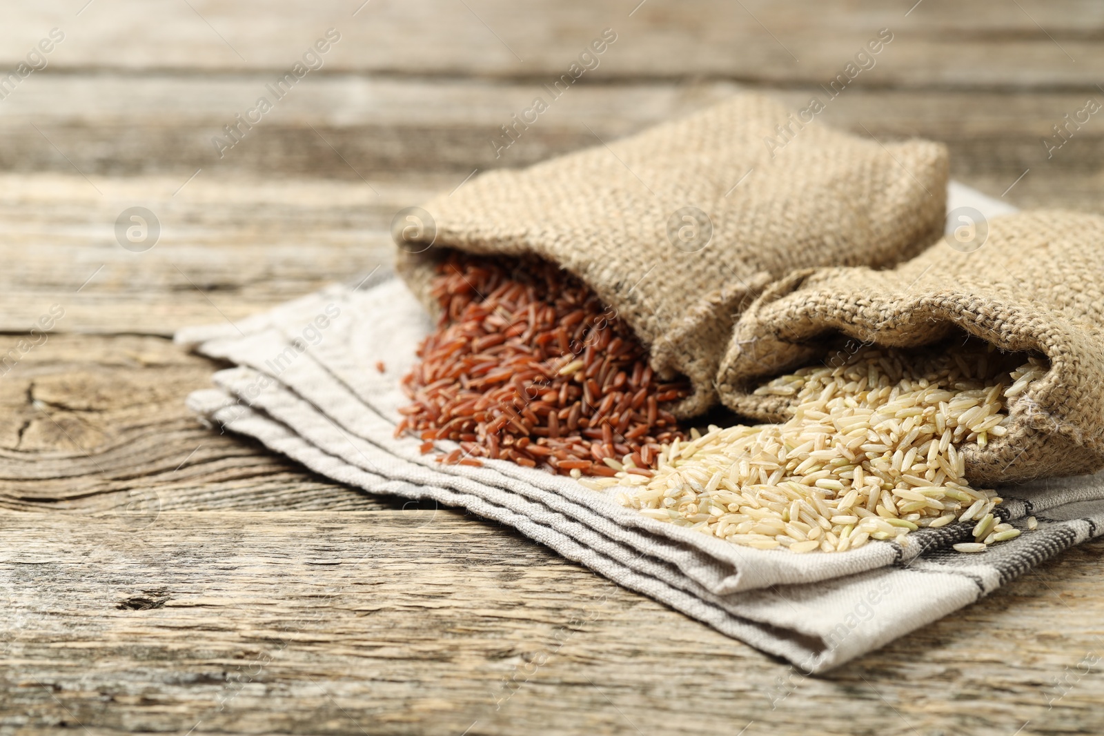 Photo of Different types of brown rice in sacks on wooden table, closeup. Space for text