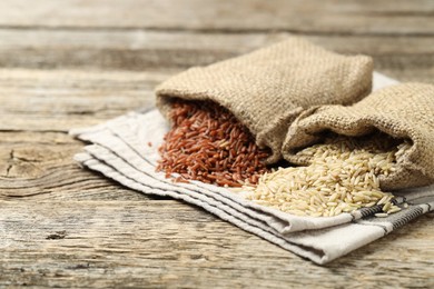 Photo of Different types of brown rice in sacks on wooden table, closeup. Space for text