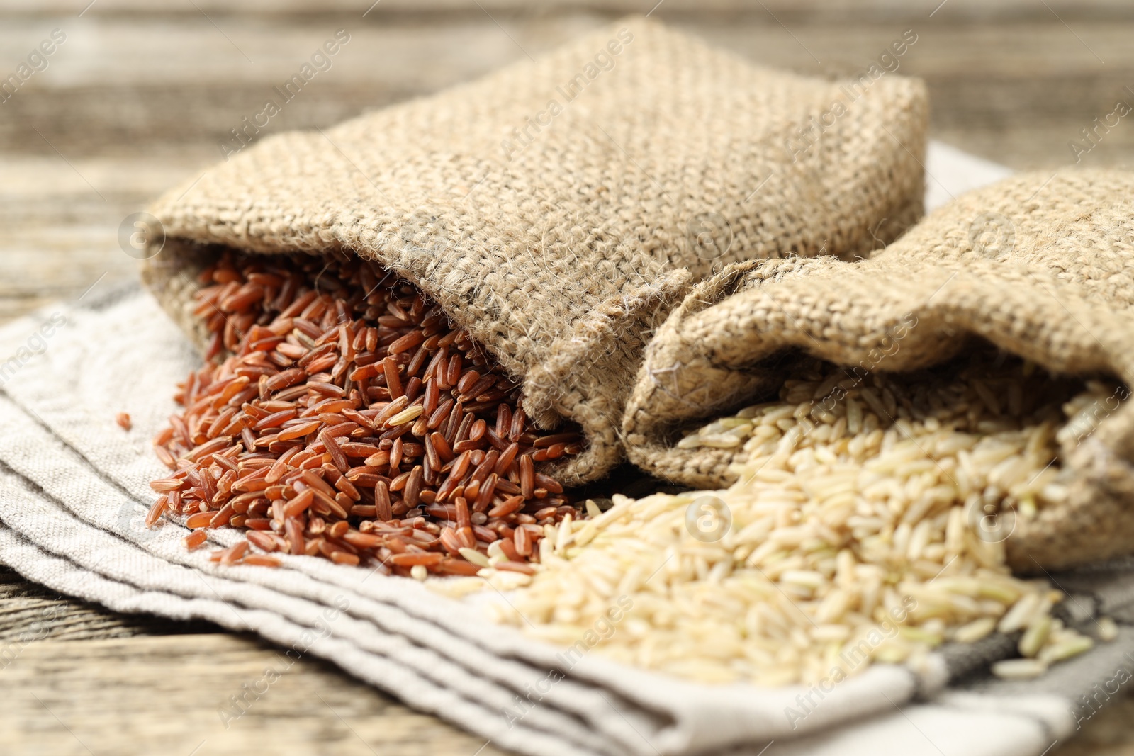 Photo of Different types of brown rice in sacks on wooden table, closeup