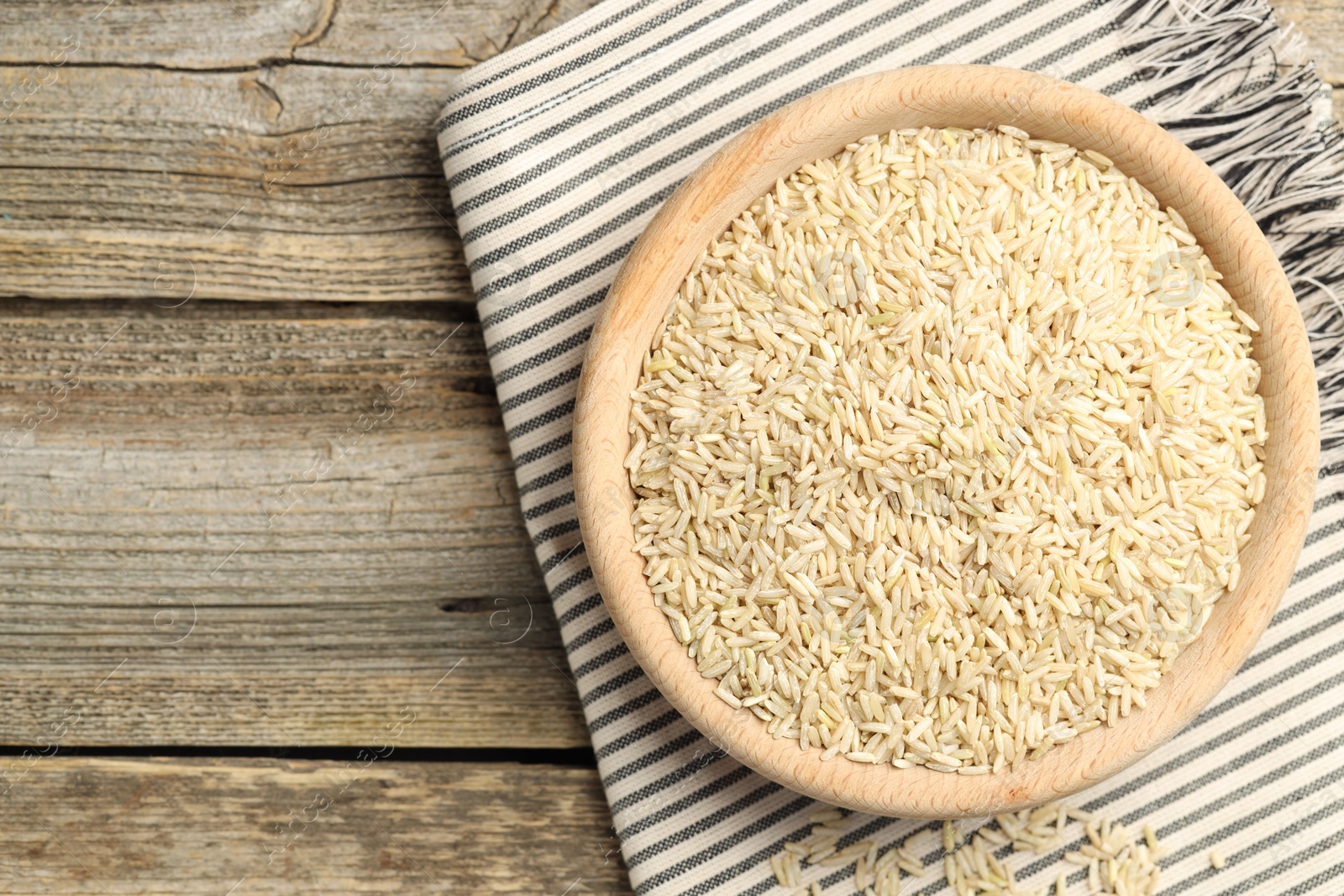 Photo of Brown rice in bowl on wooden table, top view. Space for text