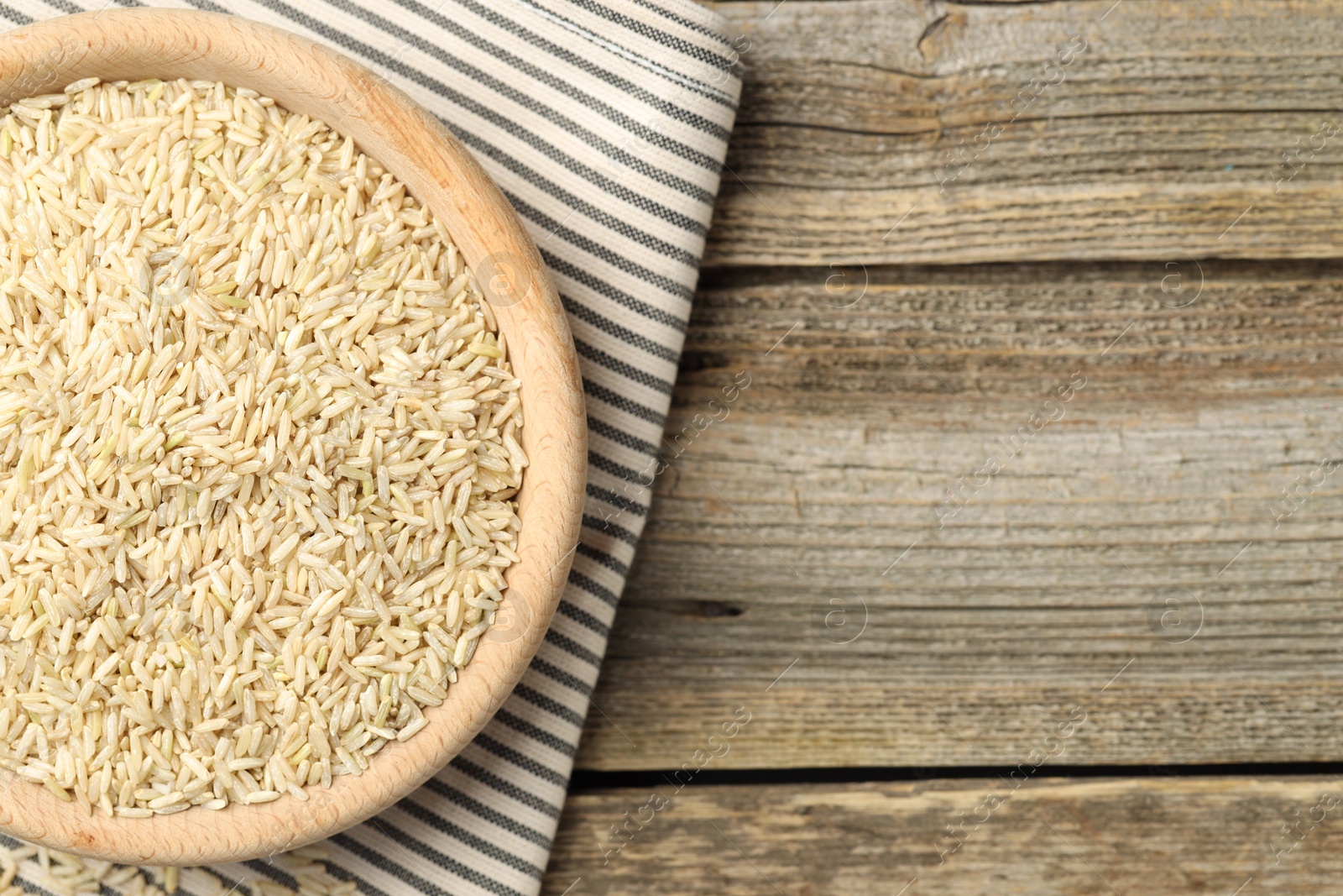 Photo of Brown rice in bowl on wooden table, top view. Space for text