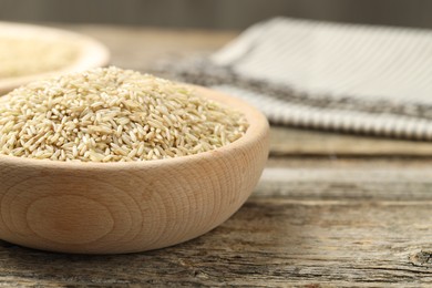 Photo of Brown rice in bowl on wooden table, closeup. Space for text