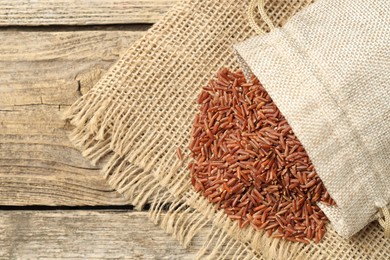 Photo of Brown rice in sack on wooden table, top view. Space for text