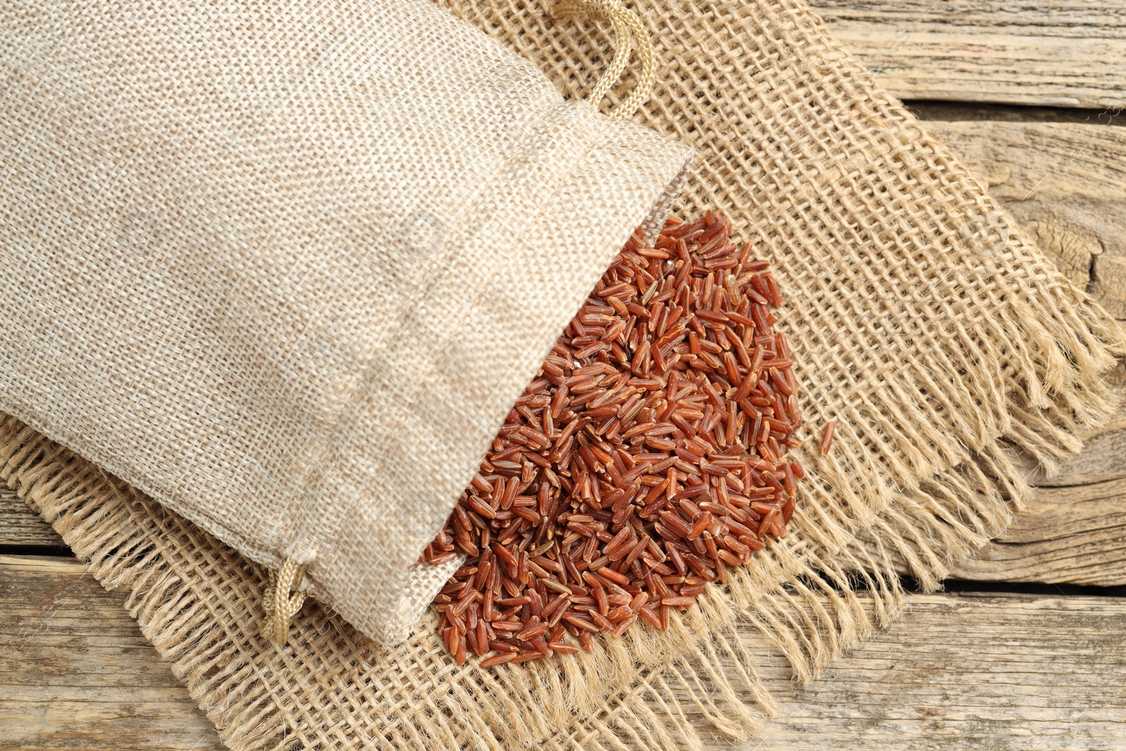 Photo of Brown rice in sack on wooden table, top view