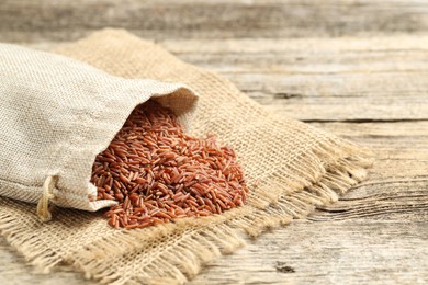 Photo of Brown rice in sack on wooden table, closeup. Space for text