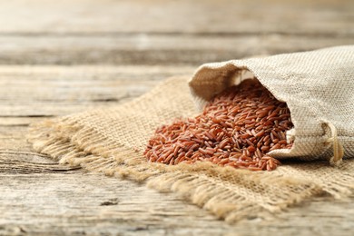 Photo of Brown rice in sack on wooden table, closeup. Space for text