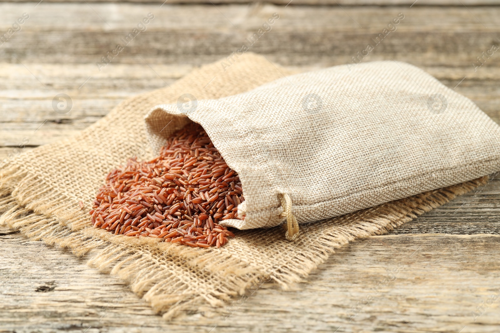 Photo of Brown rice in sack on wooden table, closeup