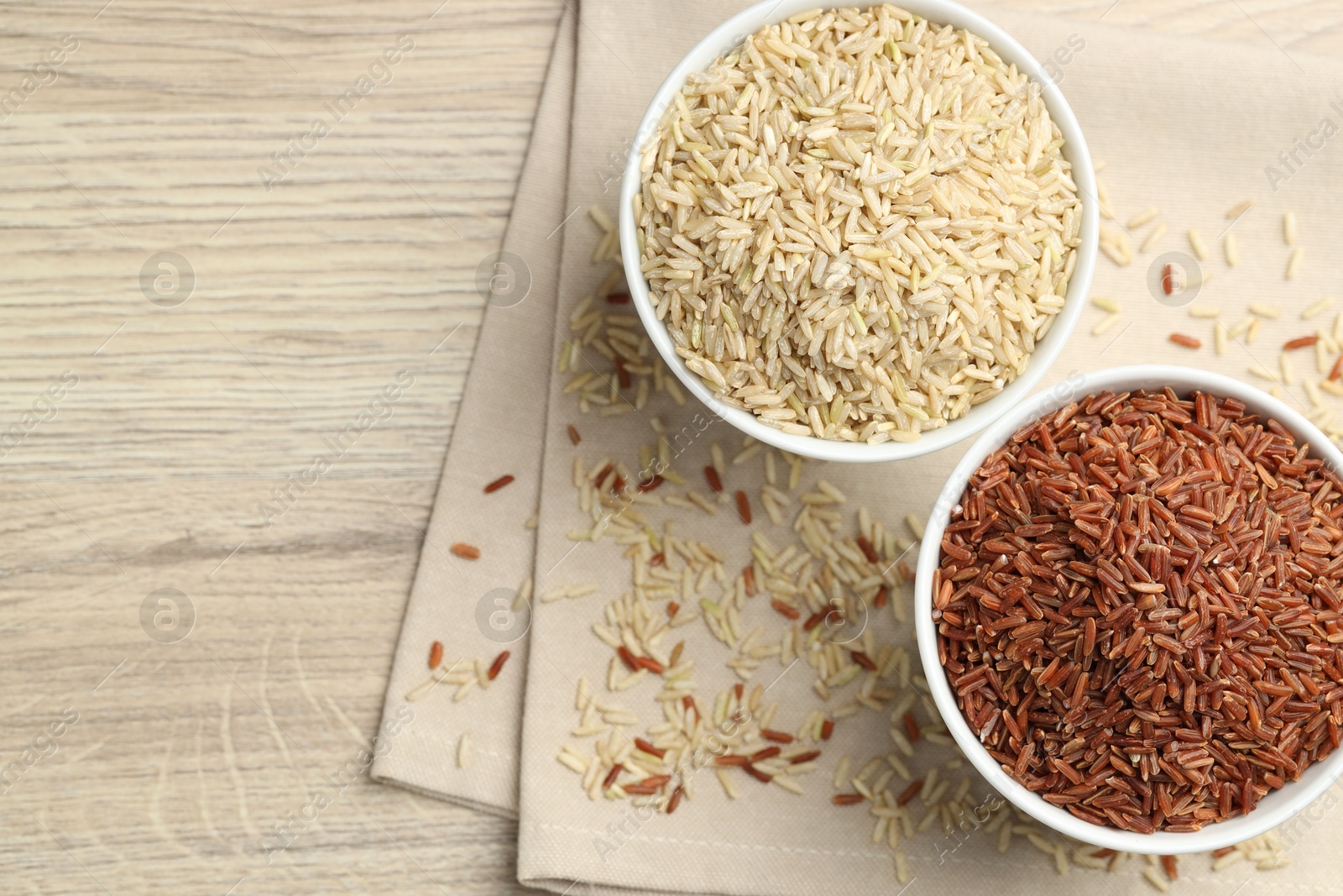 Photo of Different types of brown rice in bowls on wooden table, flat lay. Space for text