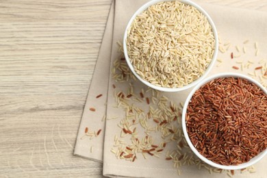 Photo of Different types of brown rice in bowls on wooden table, flat lay. Space for text