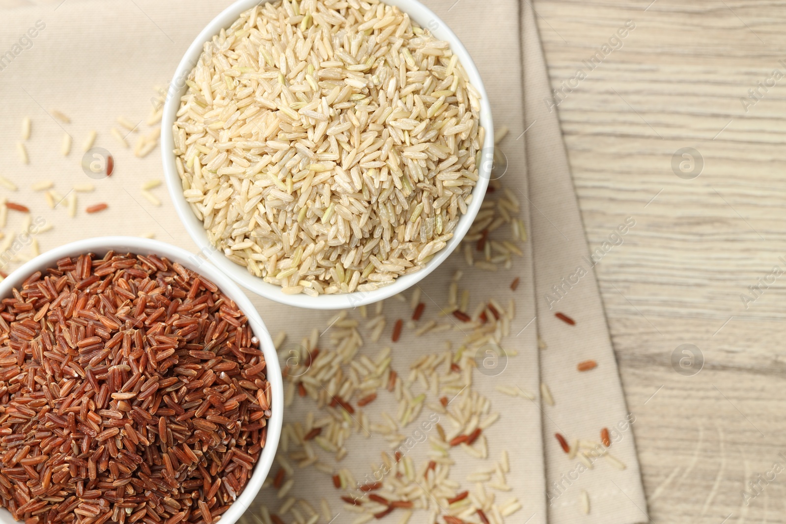 Photo of Different types of brown rice in bowls on wooden table, flat lay. Space for text