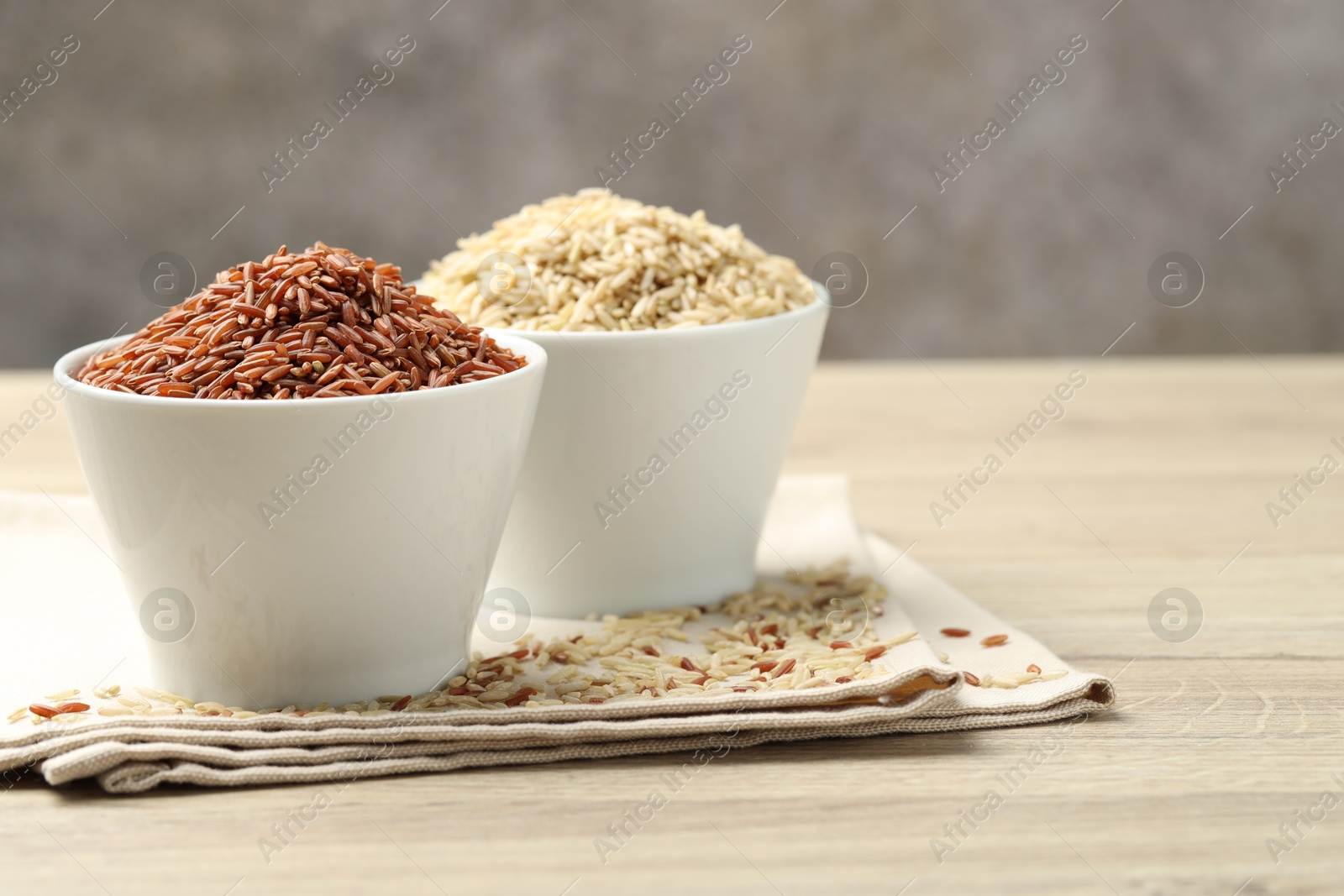 Photo of Different types of brown rice in bowls on wooden table, closeup. Space for text