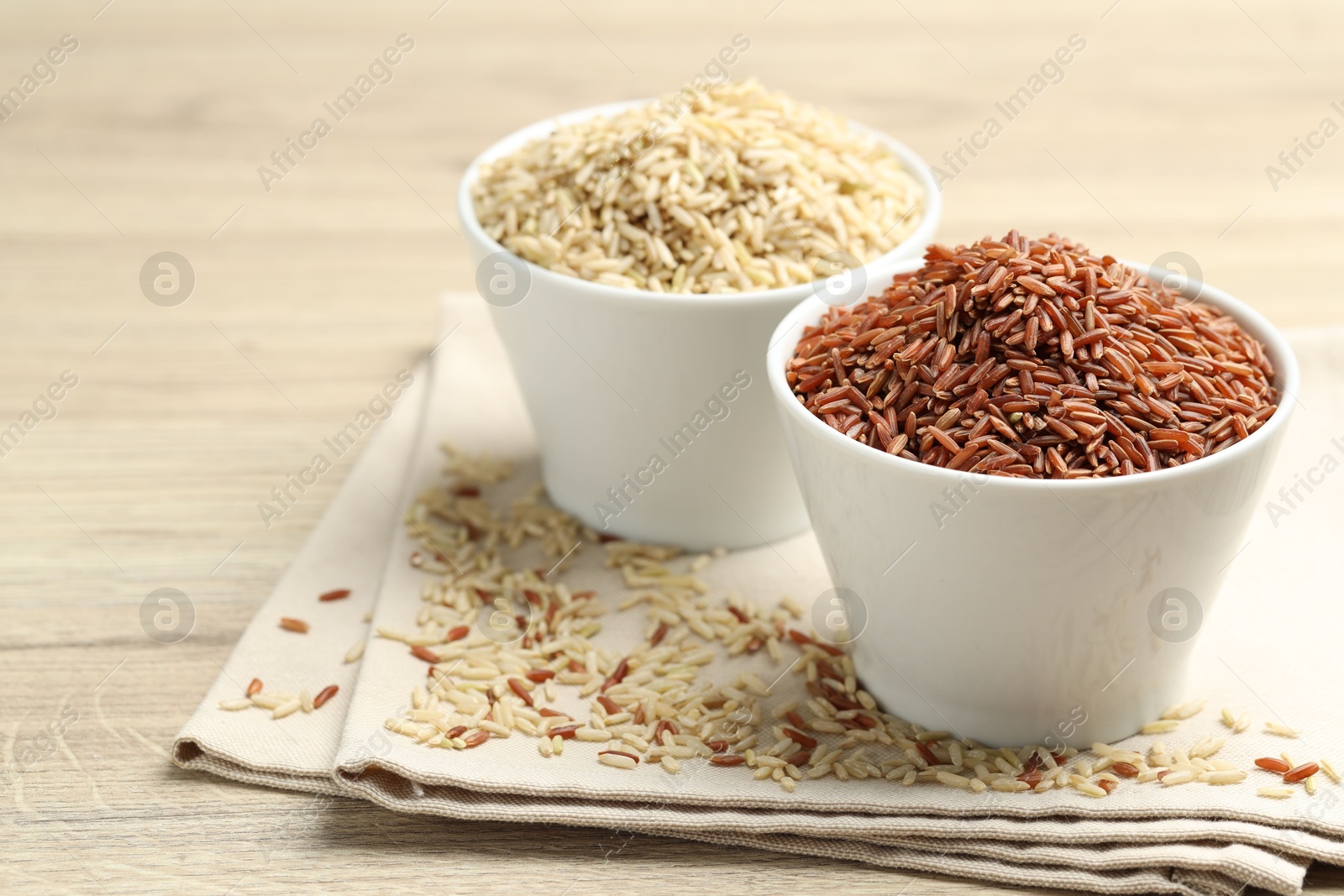 Photo of Different types of brown rice in bowls on wooden table, closeup. Space for text