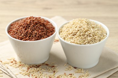 Photo of Different types of brown rice in bowls on table, closeup