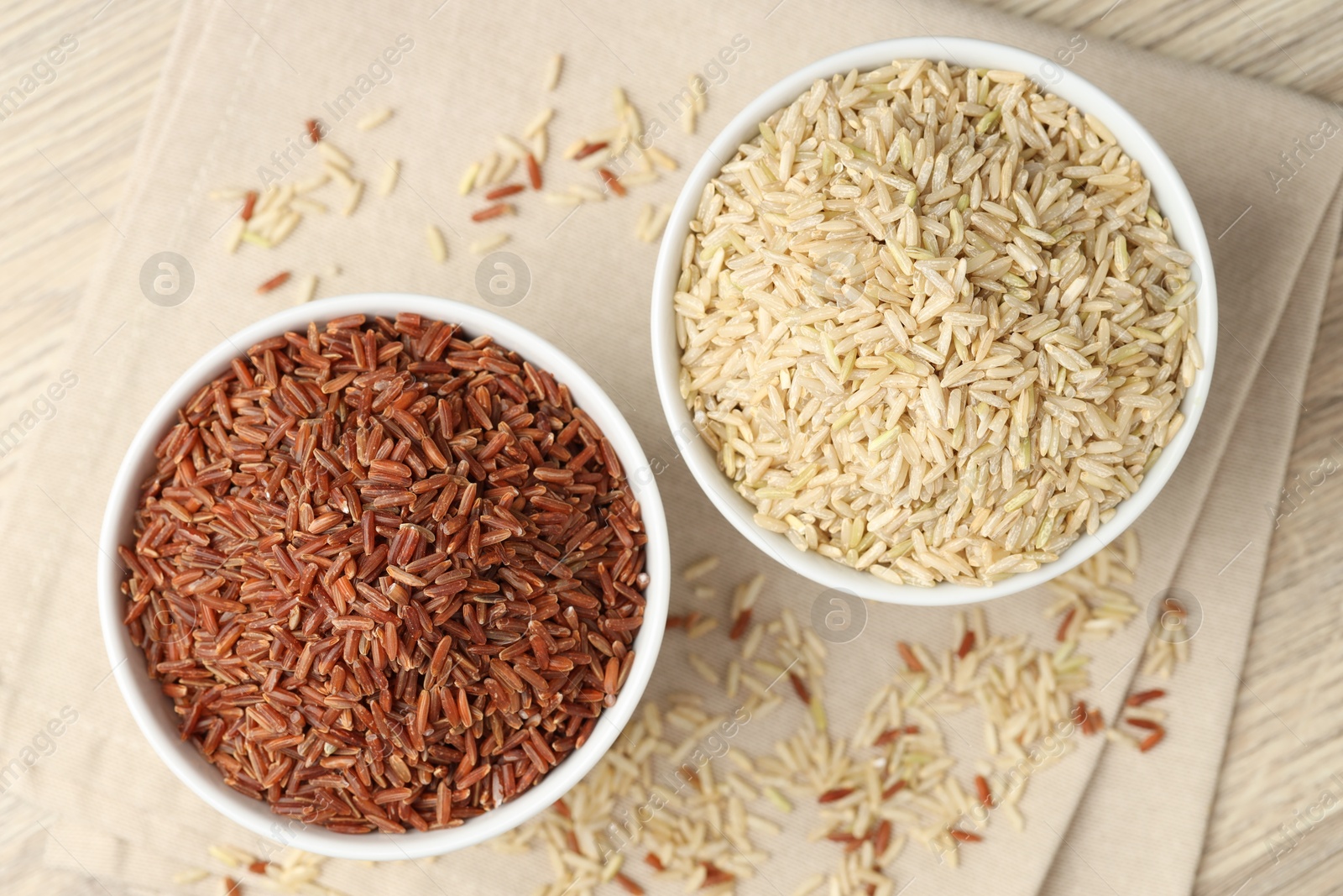 Photo of Different types of brown rice in bowls on wooden table, flat lay