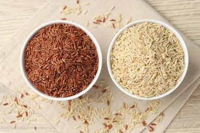 Photo of Different types of brown rice in bowls on wooden table, flat lay