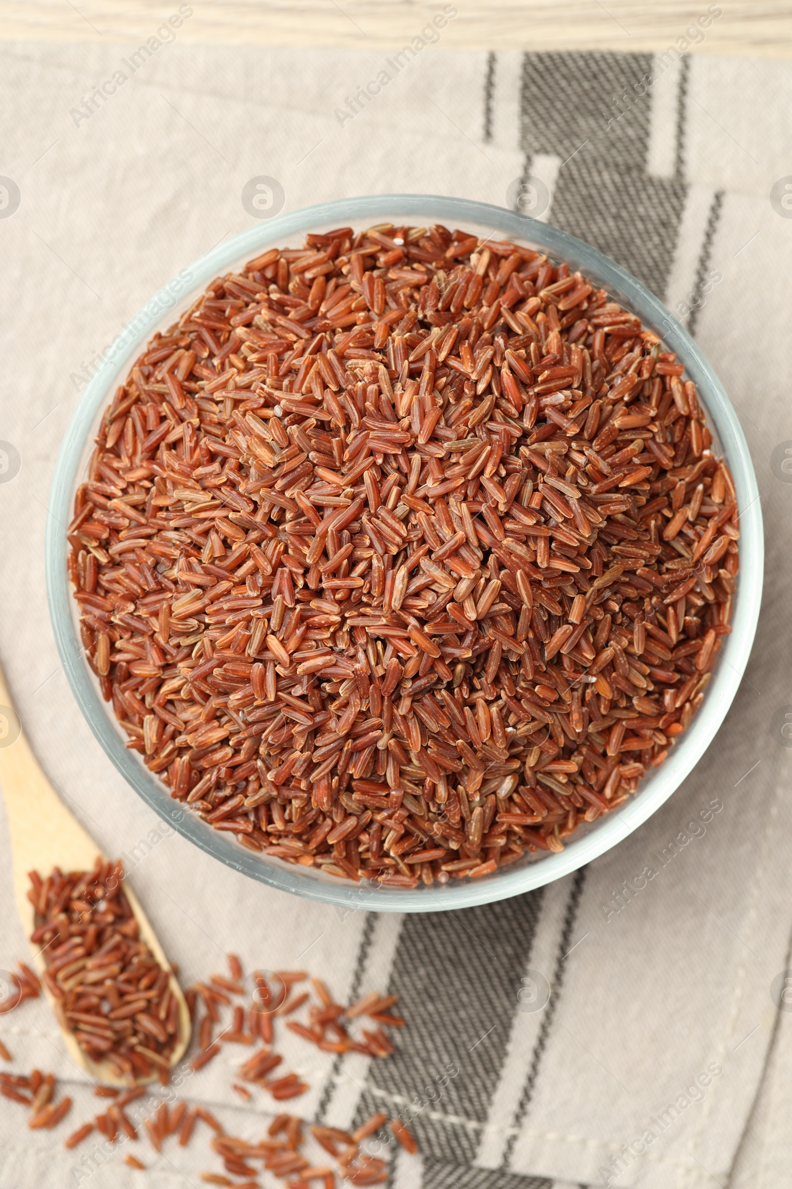 Photo of Brown rice in glass bowl and spoon on table, flat lay