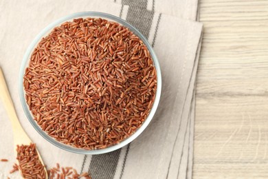 Photo of Brown rice in glass bowl and spoon on wooden table, flat lay. Space for text