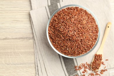 Photo of Brown rice in glass bowl and spoon on wooden table, flat lay. Space for text