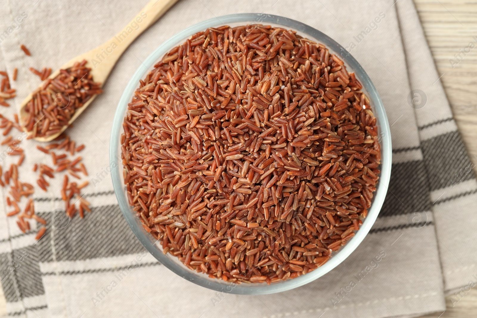 Photo of Brown rice in glass bowl and spoon on wooden table, flat lay