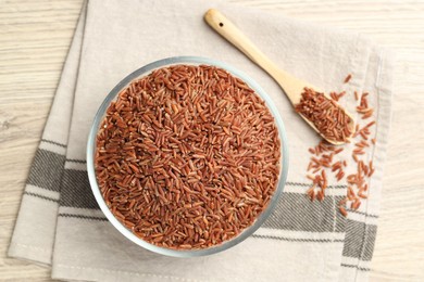 Photo of Brown rice in glass bowl and spoon on wooden table, flat lay