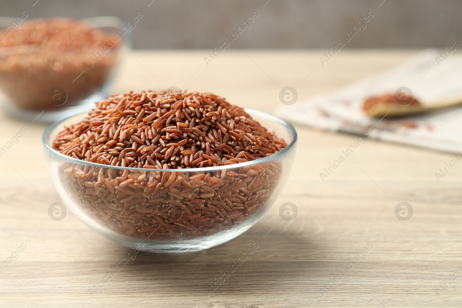 Photo of Brown rice in glass bowl on wooden table, closeup. Space for text