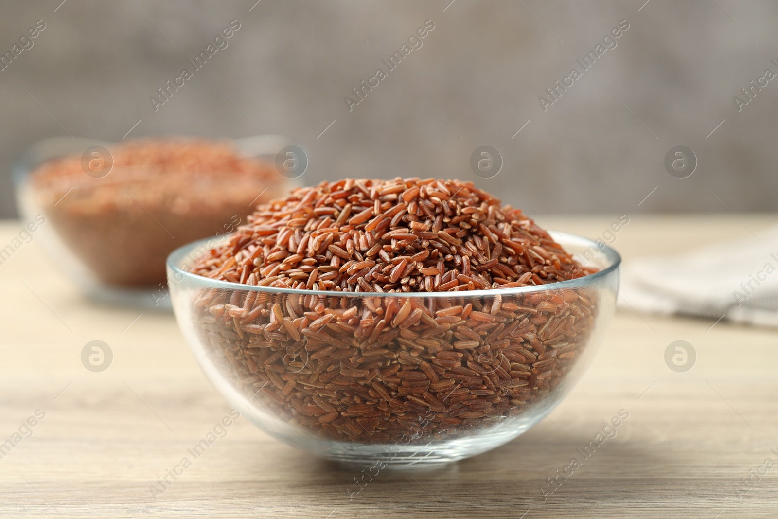 Photo of Brown rice in glass bowl on wooden table, closeup