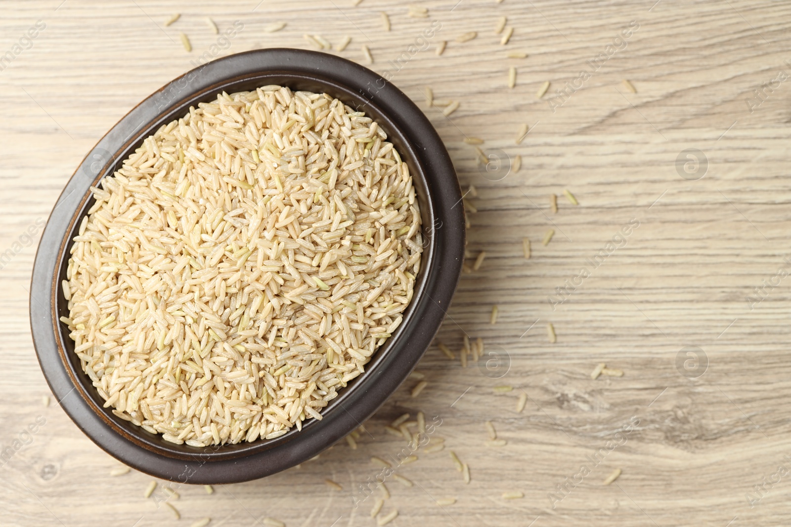 Photo of Brown rice in bowl on wooden table, top view. Space for text