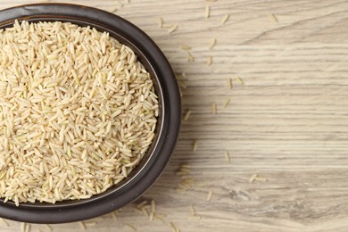 Photo of Brown rice in bowl on wooden table, top view. Space for text