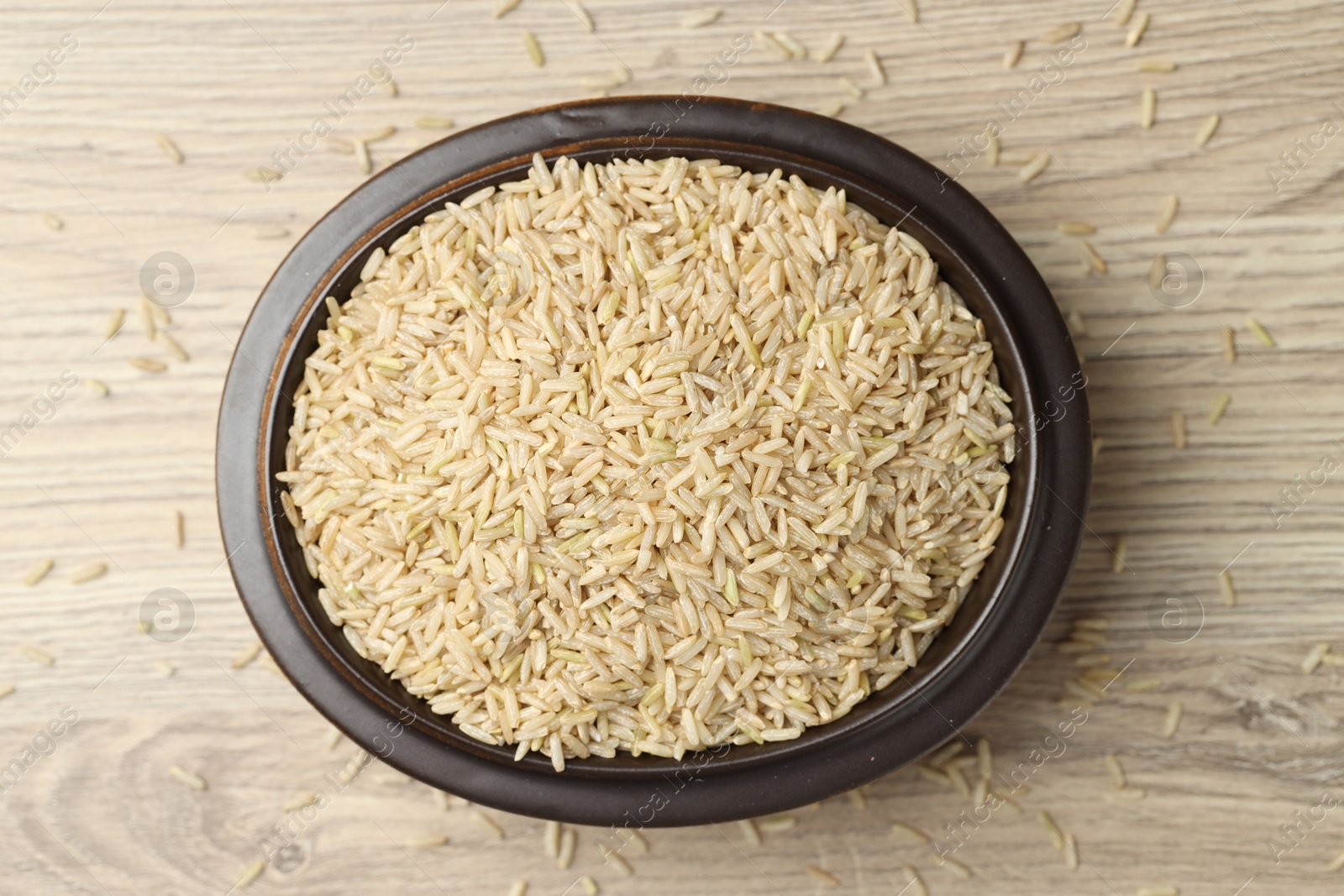 Photo of Brown rice in bowl on wooden table, top view