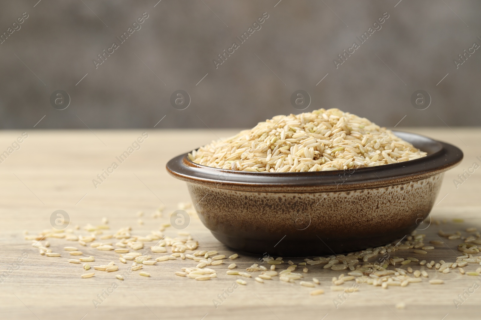 Photo of Brown rice in bowl on wooden table, closeup. Space for text